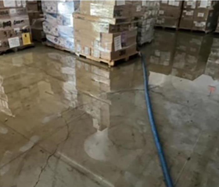 Water extraction hose in flooded warehouse with pallets waiting to be inspected